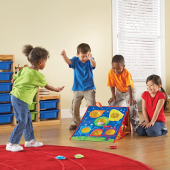 A group of children cheer as a child throws a bean bag at a board